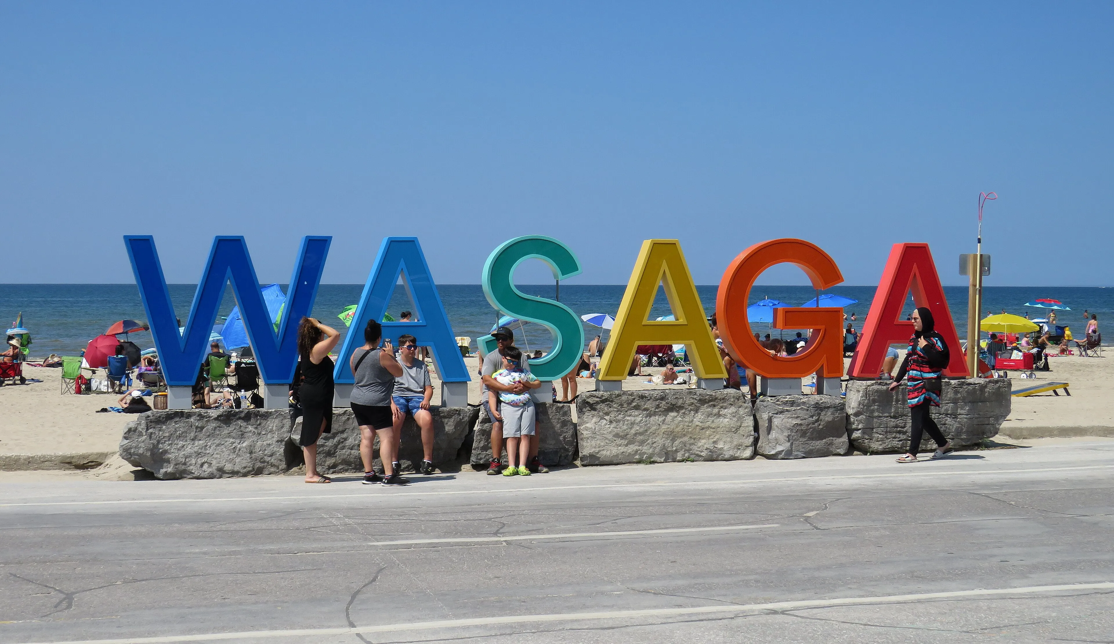 The colourful WASAGA letter sign on the beachfront, with beachgoers posing in front of it